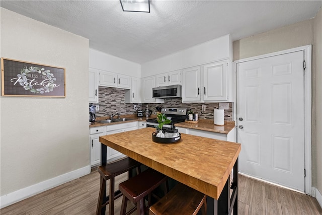 kitchen with appliances with stainless steel finishes, tasteful backsplash, wood-type flooring, sink, and white cabinets