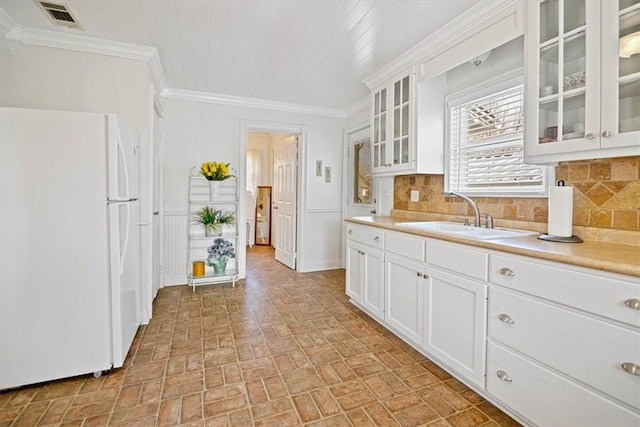 kitchen with white fridge, white cabinetry, backsplash, and sink