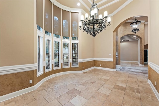 unfurnished room with a towering ceiling, ceiling fan with notable chandelier, and ornamental molding