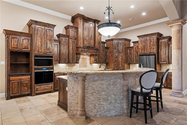 kitchen with dark brown cabinets, decorative columns, stainless steel refrigerator, and an island with sink