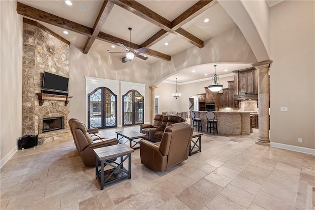 living room featuring beamed ceiling, a stone fireplace, ceiling fan, and ornate columns