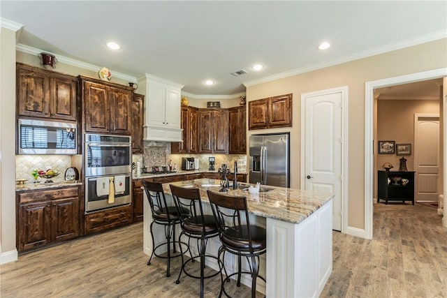 kitchen featuring a kitchen island with sink, crown molding, sink, light hardwood / wood-style flooring, and appliances with stainless steel finishes