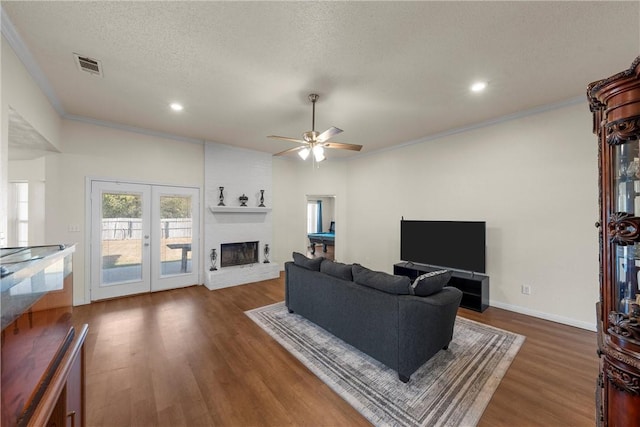 living room featuring visible vents, wood finished floors, a textured ceiling, french doors, and a brick fireplace