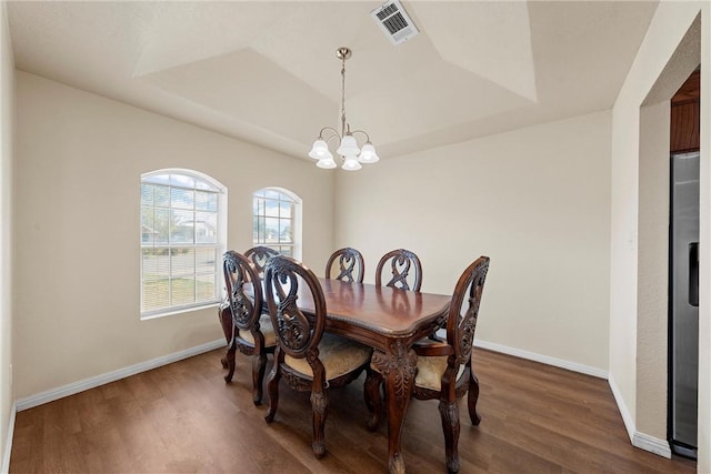 dining room with a raised ceiling, dark hardwood / wood-style flooring, and an inviting chandelier