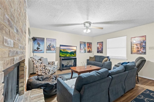 living room with wood finished floors, a textured ceiling, ceiling fan, and a fireplace