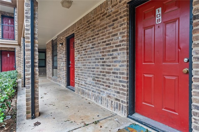 view of exterior entry featuring brick siding and covered porch