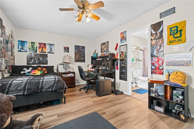 bedroom featuring a ceiling fan, wood finished floors, visible vents, a textured ceiling, and connected bathroom