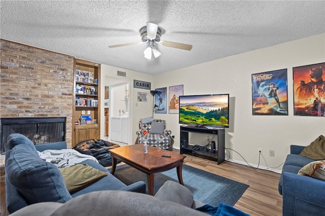 living room featuring visible vents, a ceiling fan, a textured ceiling, wood finished floors, and a brick fireplace