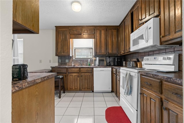 kitchen featuring white appliances, light tile patterned floors, a sink, dark countertops, and backsplash