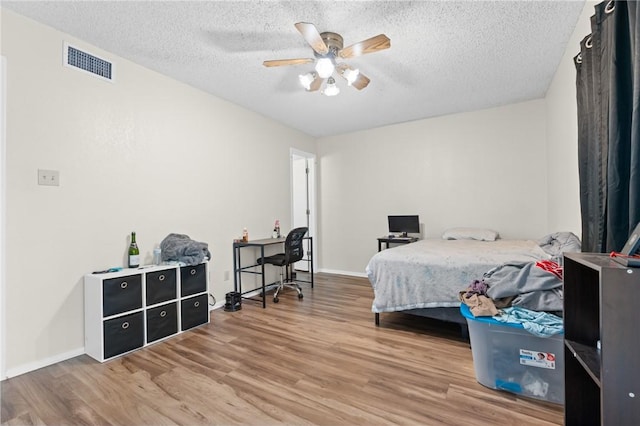 bedroom with visible vents, a textured ceiling, baseboards, and wood finished floors