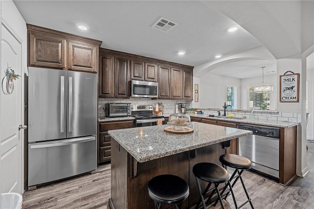 kitchen featuring hanging light fixtures, light wood-type flooring, appliances with stainless steel finishes, a kitchen island, and kitchen peninsula