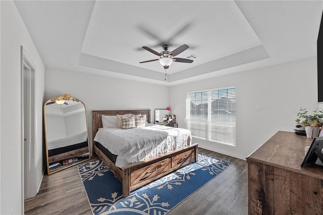 bedroom with a raised ceiling, ceiling fan, and dark wood-type flooring