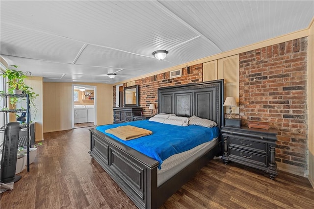 bedroom featuring separate washer and dryer, wooden walls, dark hardwood / wood-style flooring, and brick wall