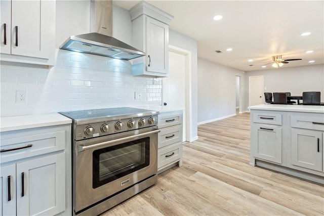 kitchen with ceiling fan, high end stainless steel range oven, wall chimney range hood, backsplash, and light hardwood / wood-style floors