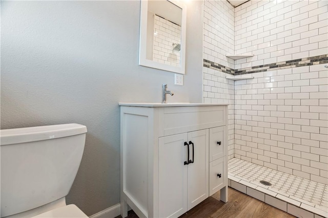 bathroom featuring tiled shower, hardwood / wood-style floors, vanity, and toilet