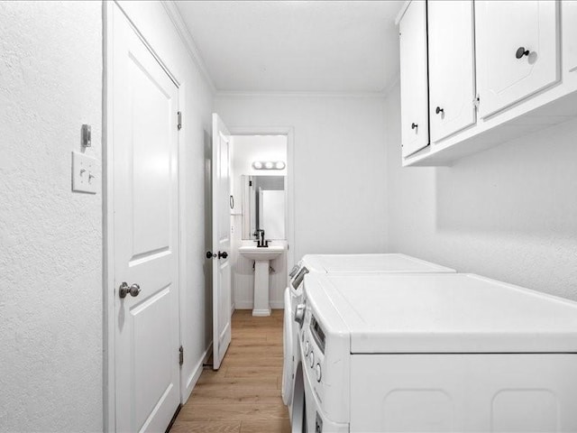 washroom featuring cabinets, washing machine and clothes dryer, crown molding, and light wood-type flooring