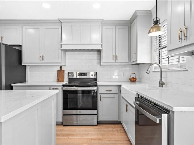 kitchen with sink, appliances with stainless steel finishes, light stone counters, decorative light fixtures, and light wood-type flooring