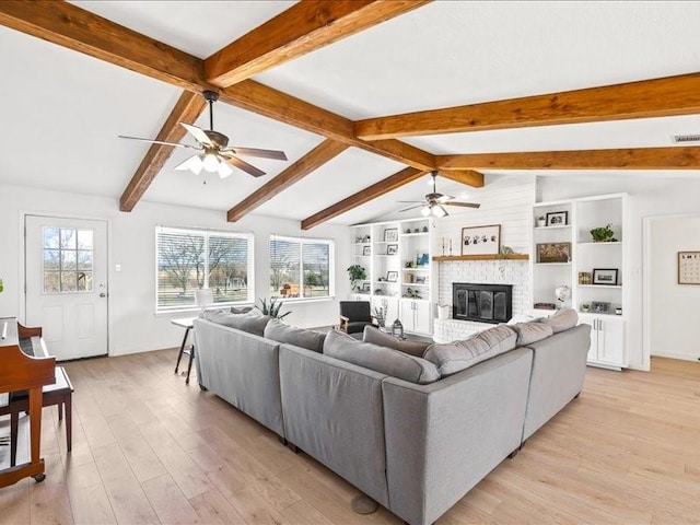 living room featuring ceiling fan, lofted ceiling with beams, a brick fireplace, and light wood-type flooring