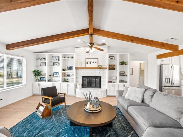 living room featuring ceiling fan, a brick fireplace, vaulted ceiling with beams, and light wood-type flooring