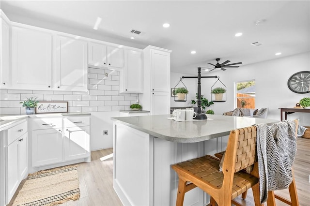 kitchen featuring decorative backsplash, white cabinetry, light hardwood / wood-style flooring, and ceiling fan