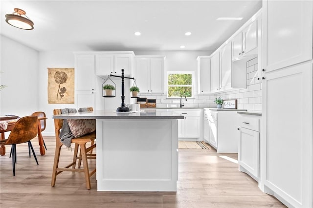 kitchen with a breakfast bar, light hardwood / wood-style flooring, white cabinets, and a kitchen island