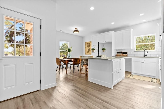 kitchen featuring sink, a kitchen island, light hardwood / wood-style flooring, backsplash, and white cabinets