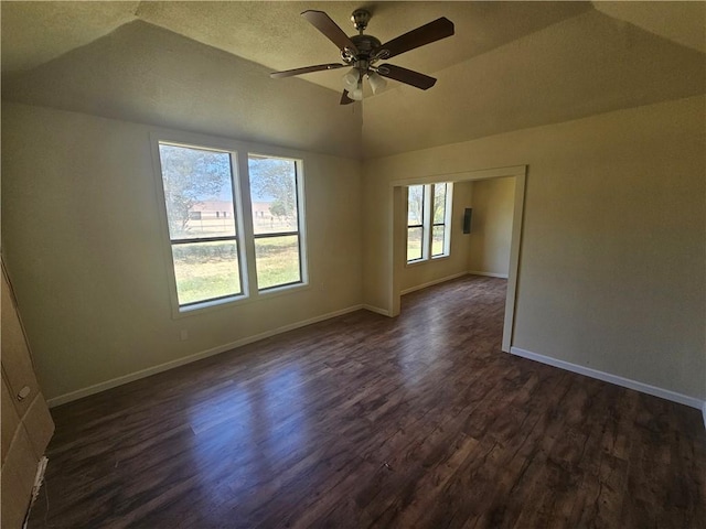 empty room with a textured ceiling, dark hardwood / wood-style floors, vaulted ceiling, and ceiling fan