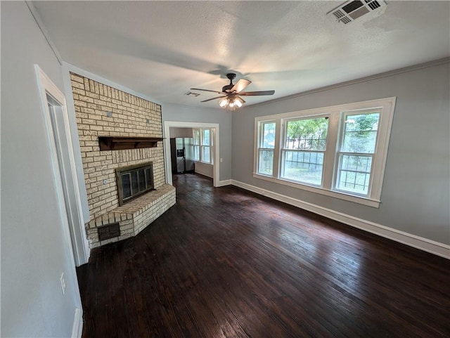 unfurnished living room featuring ceiling fan, a brick fireplace, dark hardwood / wood-style flooring, crown molding, and a textured ceiling