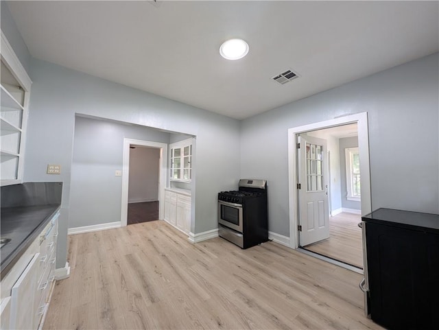 kitchen with stainless steel range with gas cooktop, white cabinets, and light hardwood / wood-style floors