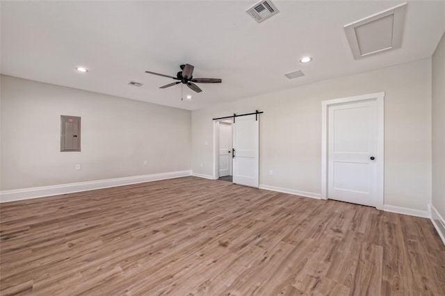 spare room with a barn door, electric panel, light hardwood / wood-style flooring, and ceiling fan