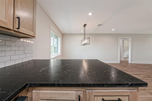 kitchen featuring light brown cabinets, backsplash, pendant lighting, dark stone counters, and light hardwood / wood-style floors