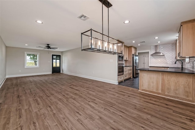 kitchen featuring appliances with stainless steel finishes, dark wood-type flooring, sink, wall chimney range hood, and decorative light fixtures