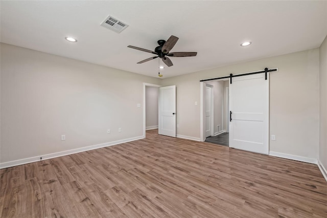 unfurnished bedroom with a barn door, ceiling fan, and light hardwood / wood-style flooring