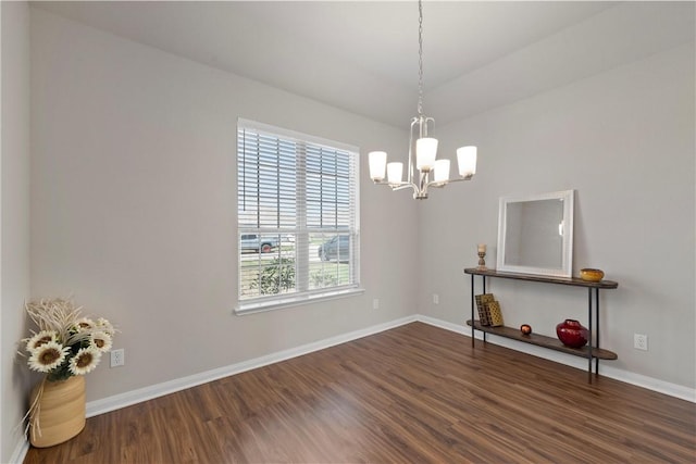 spare room featuring a chandelier and dark wood-type flooring