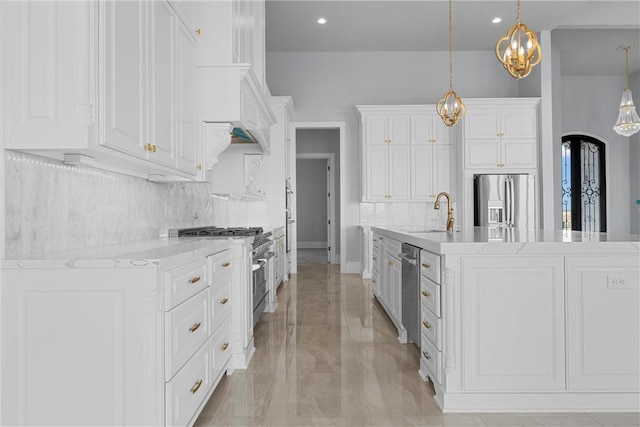 kitchen featuring sink, an island with sink, decorative light fixtures, white cabinets, and appliances with stainless steel finishes