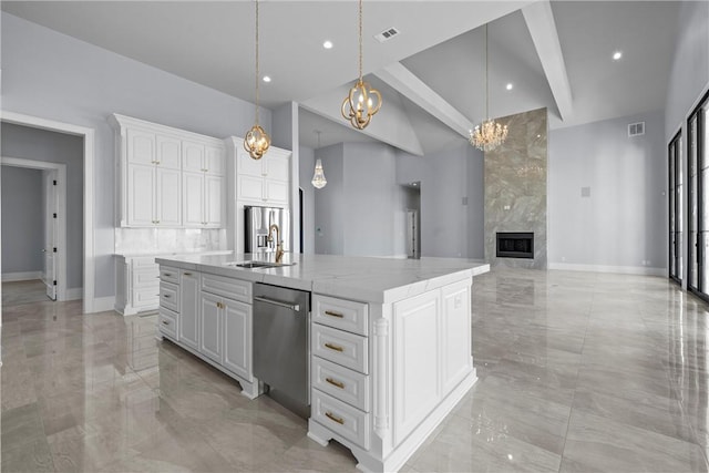 kitchen featuring light stone counters, pendant lighting, a fireplace, white cabinets, and a center island with sink