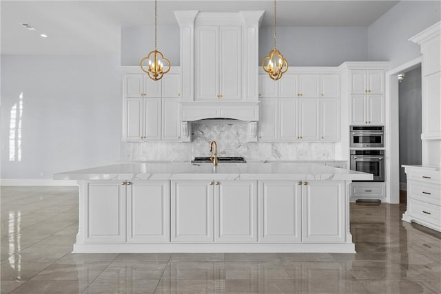 kitchen featuring stainless steel double oven, sink, decorative light fixtures, white cabinets, and an island with sink