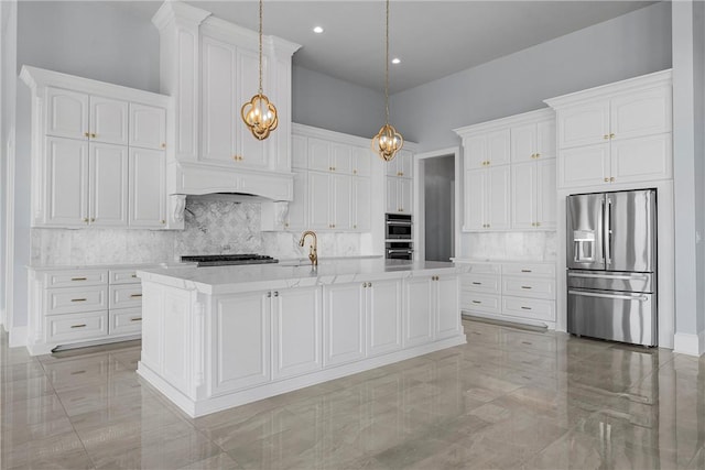 kitchen with white cabinetry, stainless steel appliances, hanging light fixtures, and an island with sink