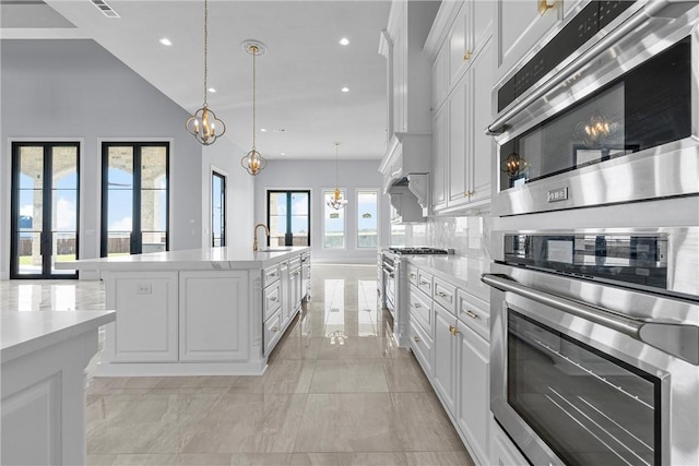 kitchen featuring hanging light fixtures, decorative backsplash, a center island with sink, white cabinets, and appliances with stainless steel finishes