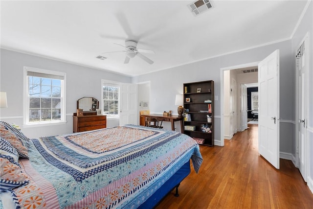 bedroom with a ceiling fan, visible vents, baseboards, and wood finished floors