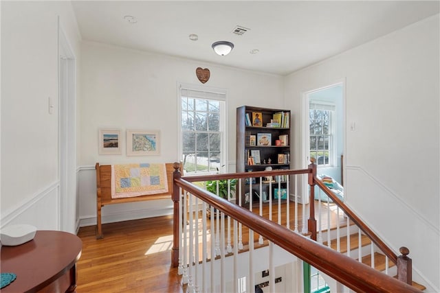 hall featuring light wood-style floors, baseboards, visible vents, and an upstairs landing