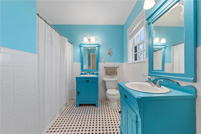 full bath featuring a shower with shower curtain, toilet, a wainscoted wall, vanity, and tile walls