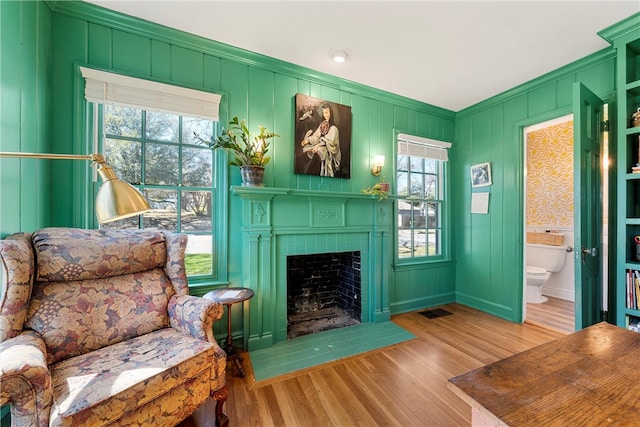 sitting room with wood finished floors, visible vents, baseboards, a tiled fireplace, and crown molding