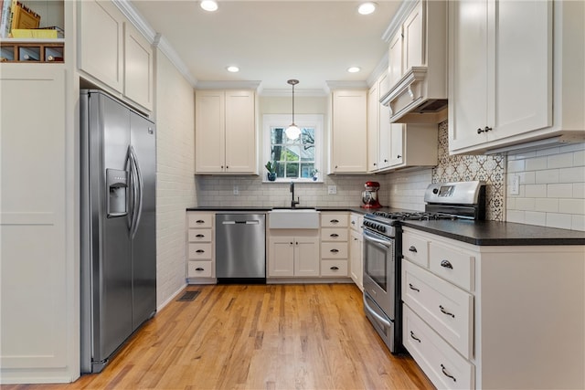 kitchen with crown molding, light wood finished floors, dark countertops, decorative backsplash, and appliances with stainless steel finishes