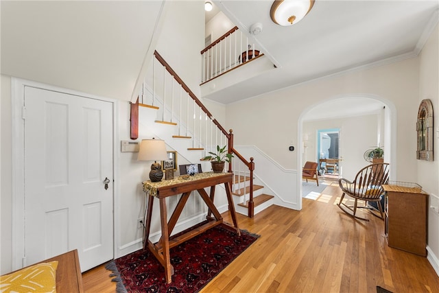 foyer entrance with arched walkways, light wood-style flooring, baseboards, ornamental molding, and stairway