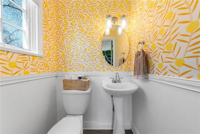 bathroom featuring a wainscoted wall, a sink, toilet, and wallpapered walls