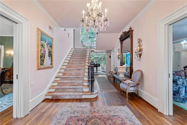 foyer entrance with hardwood / wood-style floors, crown molding, and a notable chandelier