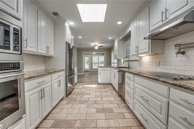 kitchen featuring a skylight, sink, stainless steel appliances, stone countertops, and white cabinets