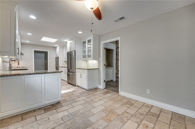 kitchen with white cabinets, sink, a skylight, appliances with stainless steel finishes, and tasteful backsplash