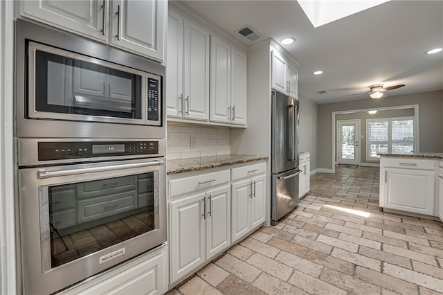 kitchen featuring white cabinets, decorative backsplash, ceiling fan, appliances with stainless steel finishes, and light stone counters